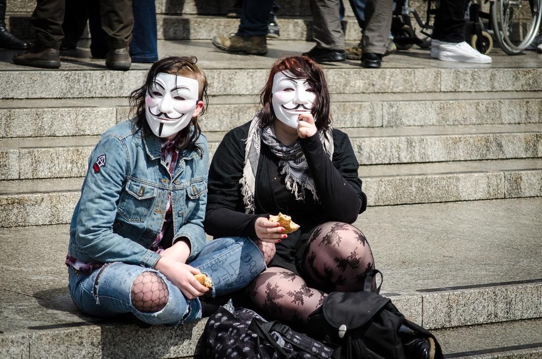 Två personer med Anonymous-masker som sitter på en trappa.